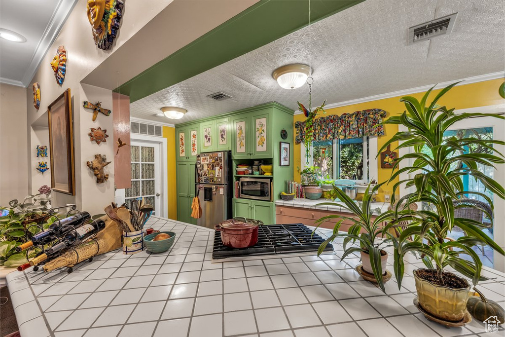 Kitchen with tile countertops, appliances with stainless steel finishes, green cabinetry, and ornamental molding