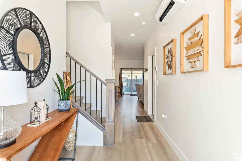 Hall with wood finished floors, an AC wall unit, recessed lighting, stairway, and baseboards