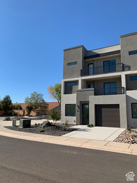 View of front of house with a balcony, stucco siding, driveway, and a garage