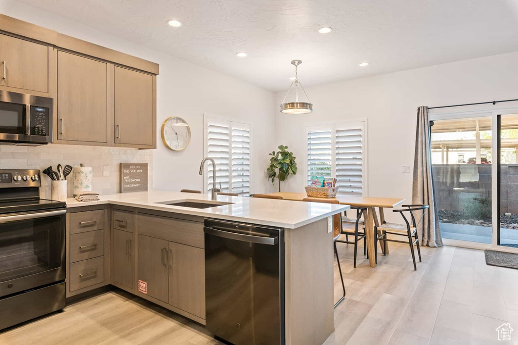 Kitchen featuring stainless steel appliances, a sink, a peninsula, light wood finished floors, and recessed lighting