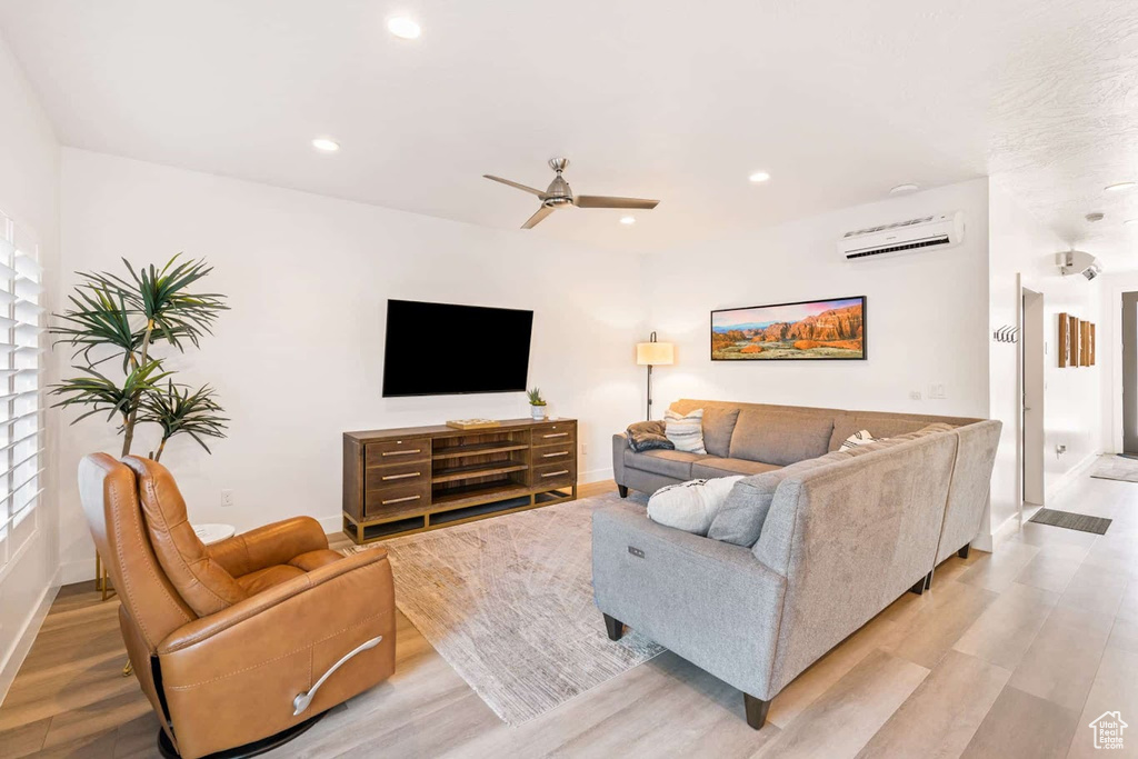 Living room featuring light wood finished floors, baseboards, a wall unit AC, and recessed lighting