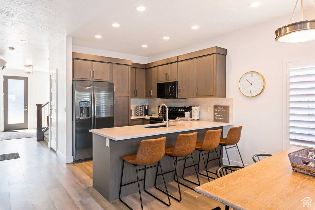 Kitchen featuring black appliances, a peninsula, a sink, backsplash, and recessed lighting
