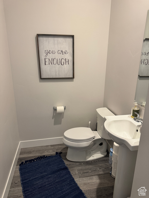 Half bathroom featuring wood finished floors, toilet, and baseboards
