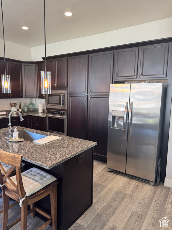 Kitchen featuring appliances with stainless steel finishes, a sink, stone counters, light wood-style flooring, and pendant lighting