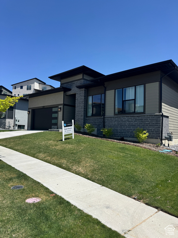View of front facade featuring an attached garage, a front lawn, and brick siding