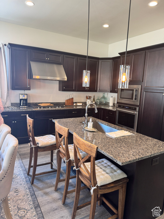 Kitchen with stainless steel appliances, under cabinet range hood, a sink, dark stone counters, and recessed lighting