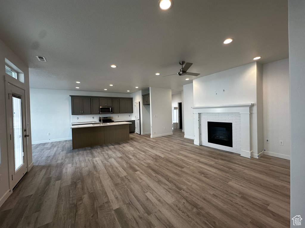 Unfurnished living room featuring wood finished floors, baseboards, a ceiling fan, recessed lighting, and a fireplace