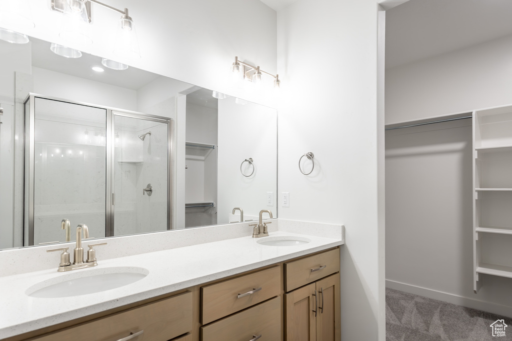 Full bath featuring a walk in closet, double vanity, a shower stall, and baseboards
