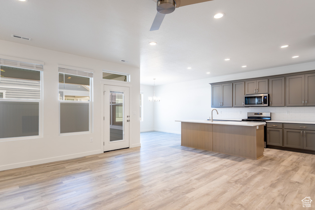 Kitchen with stainless steel appliances, tasteful backsplash, a center island with sink, ceiling fan, and light wood-style flooring