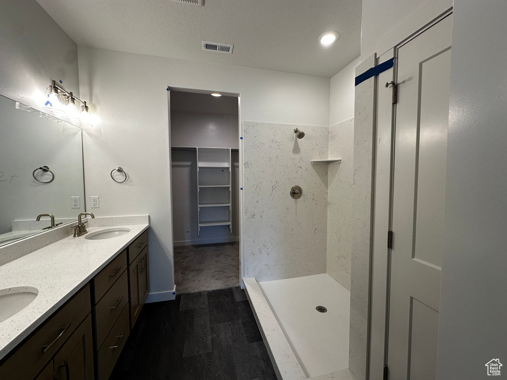 Full bath with a tile shower, wood finished floors, double vanity, and a walk in closet