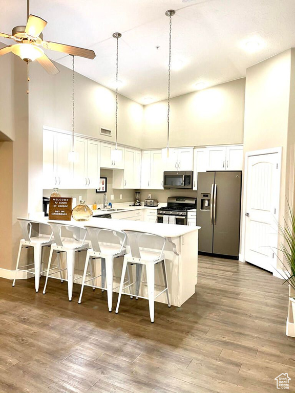Kitchen featuring a peninsula, appliances with stainless steel finishes, a kitchen breakfast bar, and high vaulted ceiling
