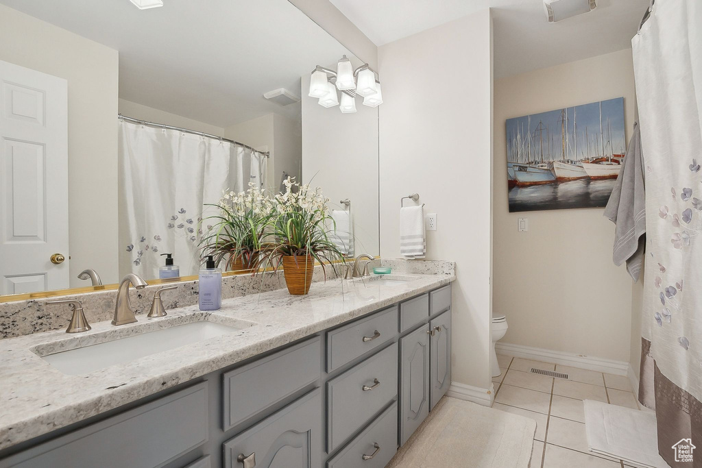 Full bathroom featuring toilet, double vanity, tile patterned floors, and baseboards