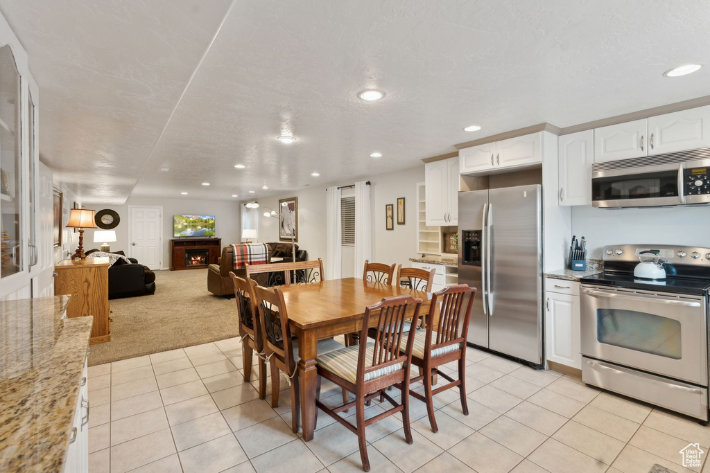 Dining area featuring light tile patterned floors, light colored carpet, recessed lighting, and a lit fireplace