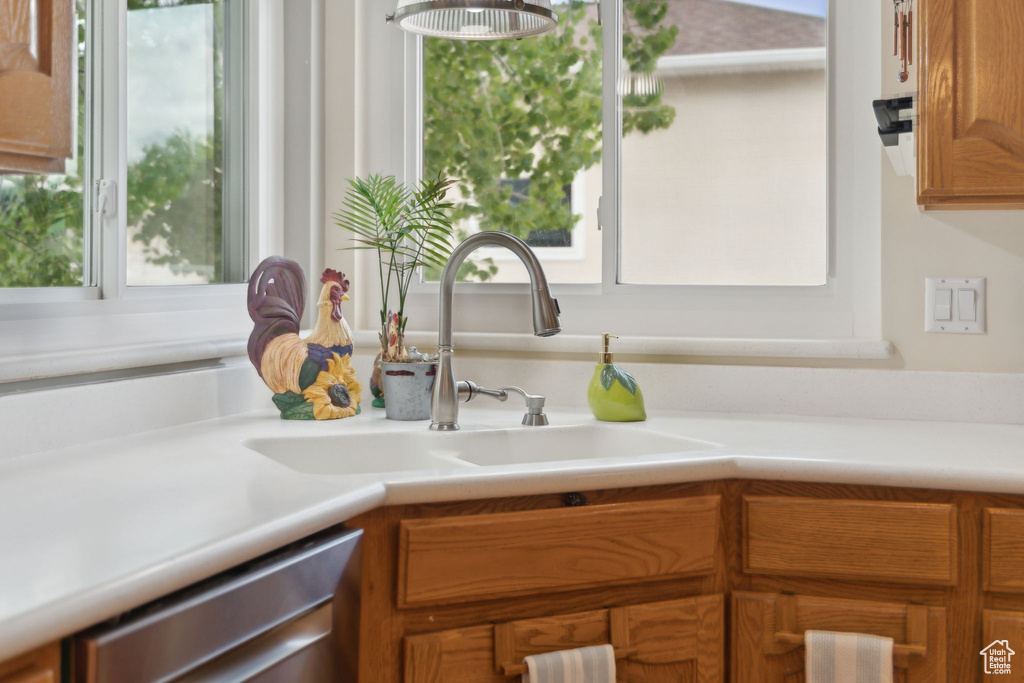 Kitchen with a sink, dishwasher, light countertops, and brown cabinets