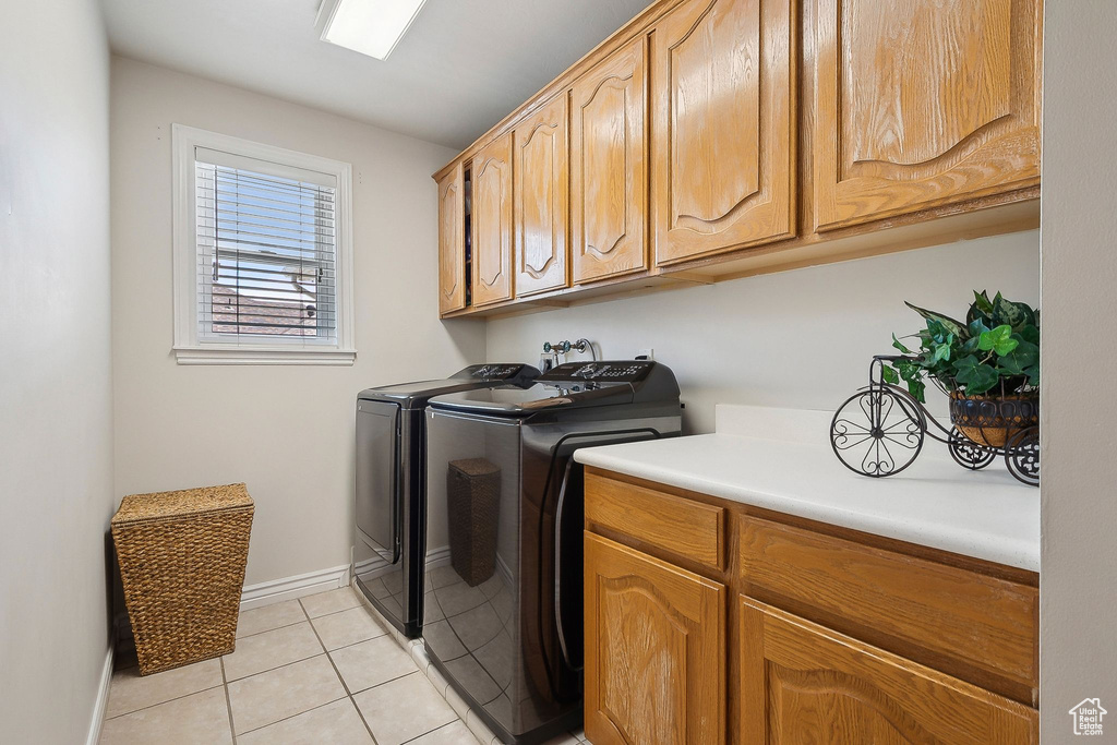 Laundry area featuring separate washer and dryer, cabinet space, light tile patterned flooring, and baseboards