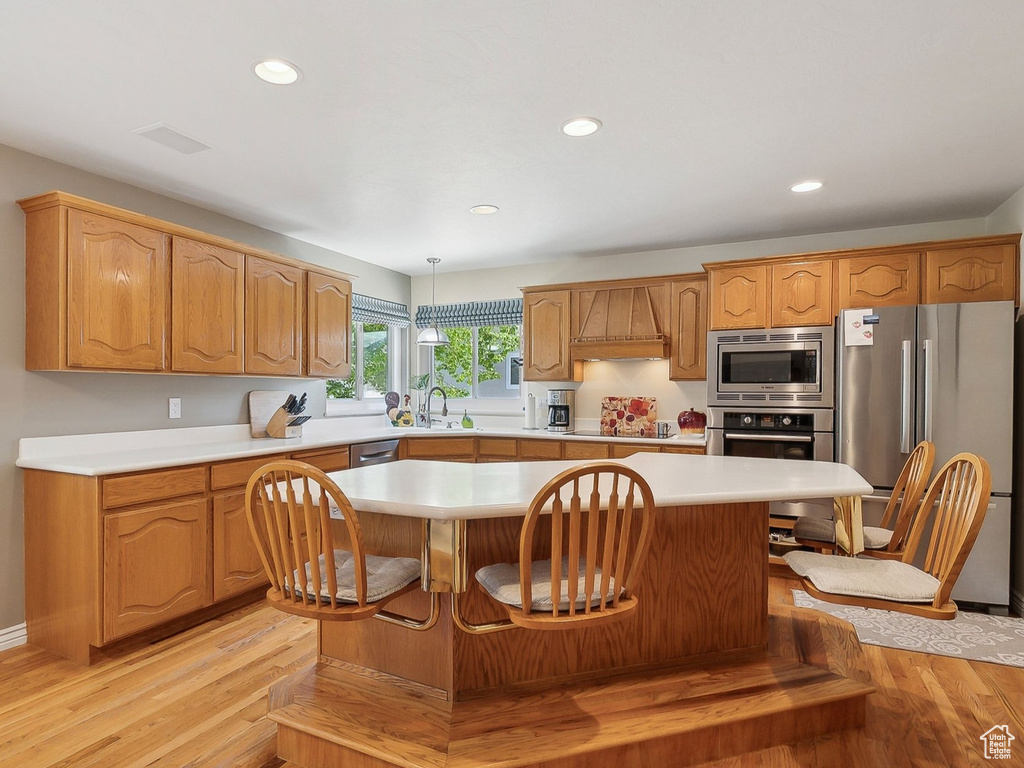 Kitchen featuring stainless steel appliances, a kitchen island, light countertops, light wood-style flooring, and baseboards