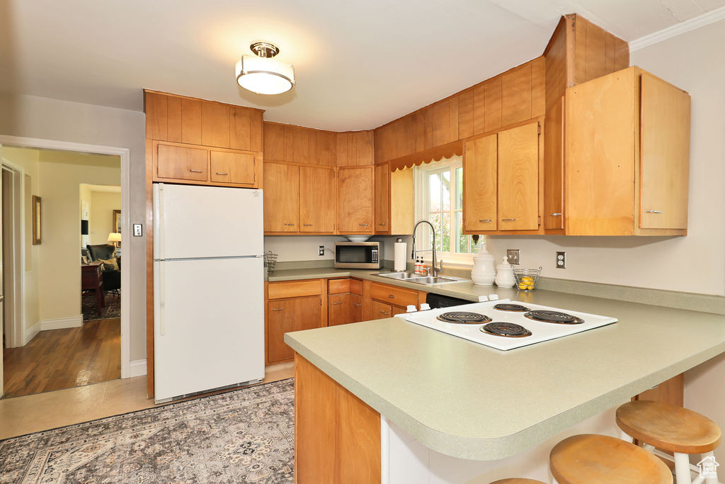 Kitchen featuring white appliances, a sink, a peninsula, a kitchen breakfast bar, and light countertops