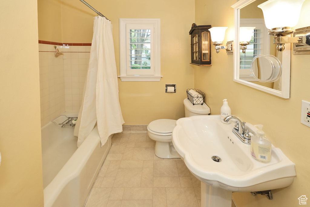 Full bathroom featuring toilet, a sink, baseboards, shower / bath combo, and tile patterned flooring