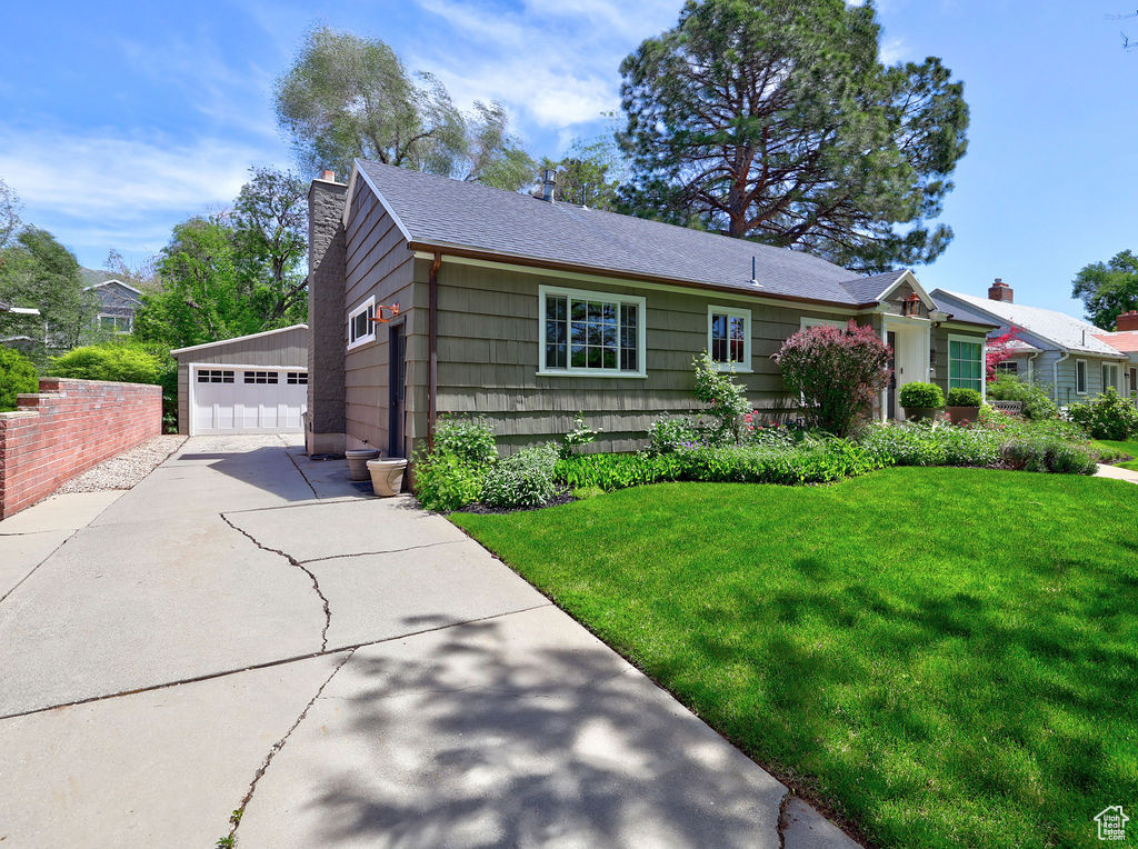 Single story home featuring a chimney, a garage, a front lawn, and a shingled roof