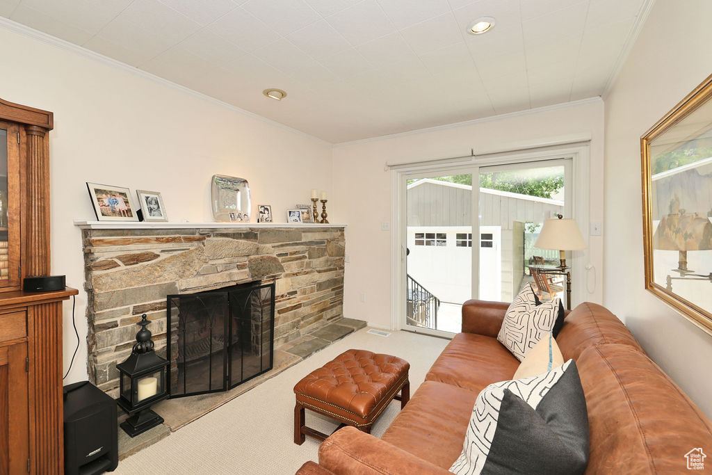 Carpeted living area with ornamental molding, a stone fireplace, and recessed lighting