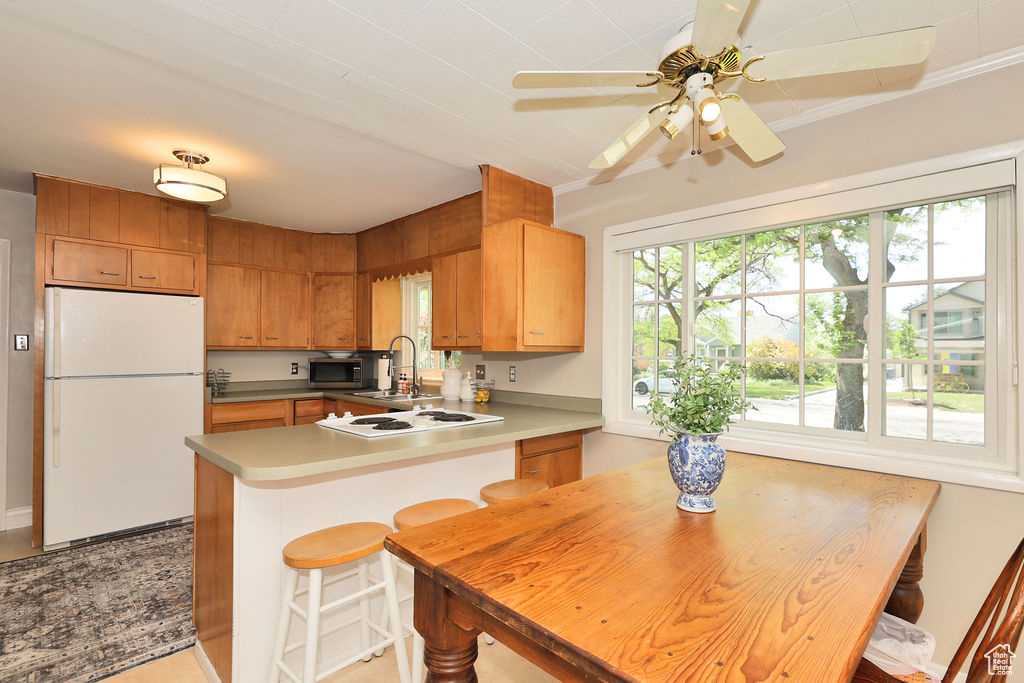 Kitchen featuring white appliances, a sink, a peninsula, a ceiling fan, and brown cabinets
