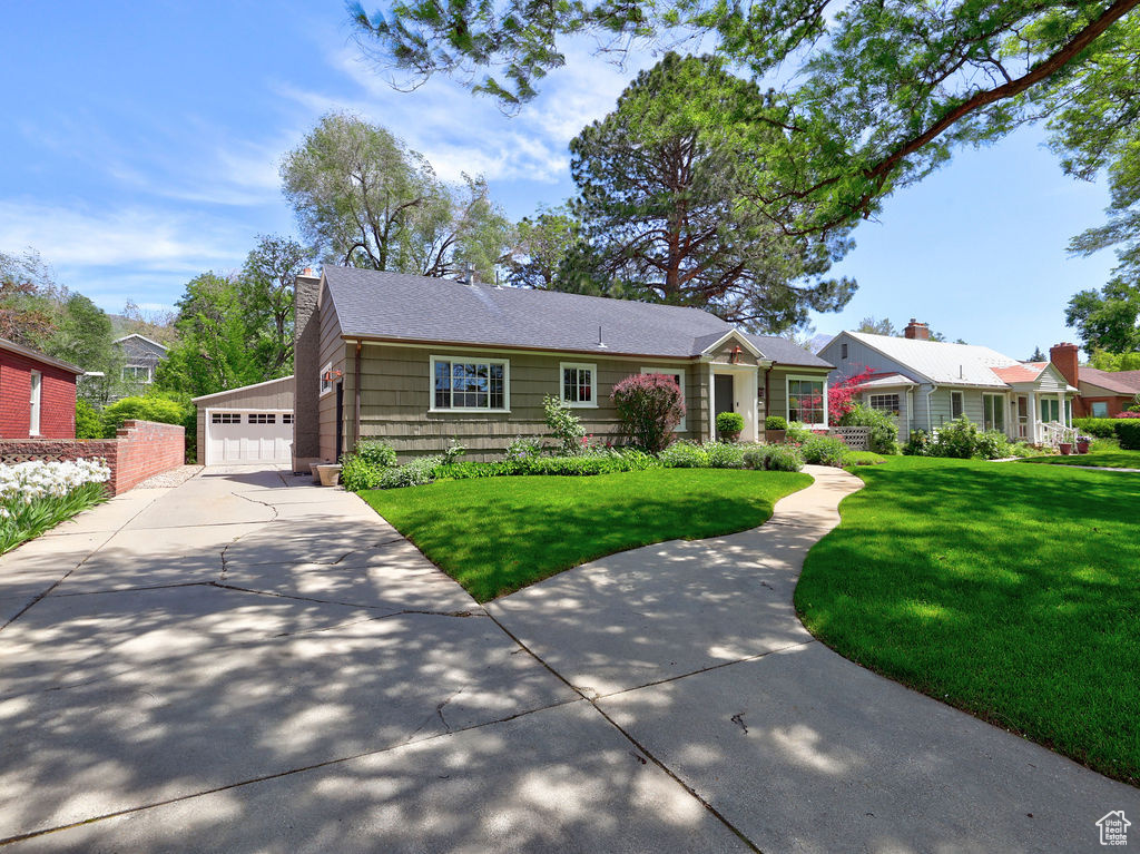 Ranch-style home featuring a detached garage, a chimney, and a front yard