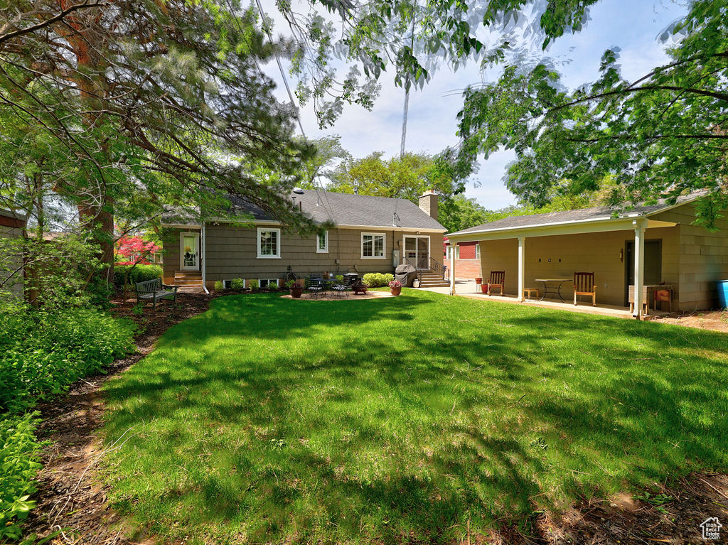 Rear view of property featuring entry steps, a patio area, a chimney, and a yard