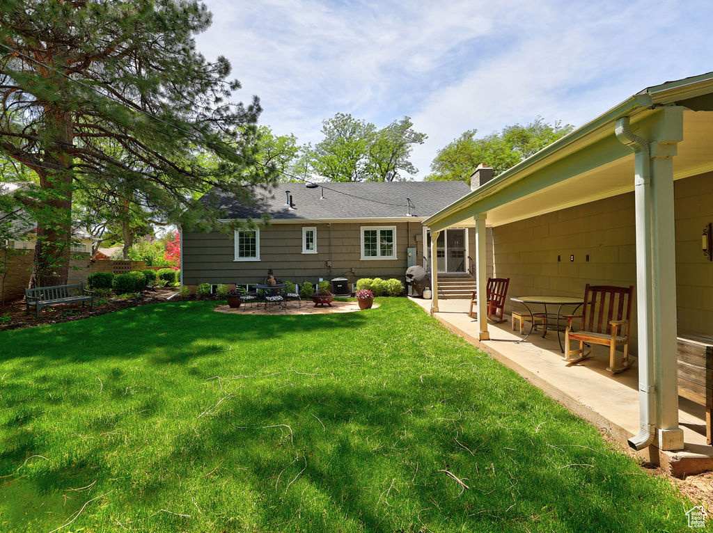 Rear view of house with a patio, entry steps, a lawn, and a chimney