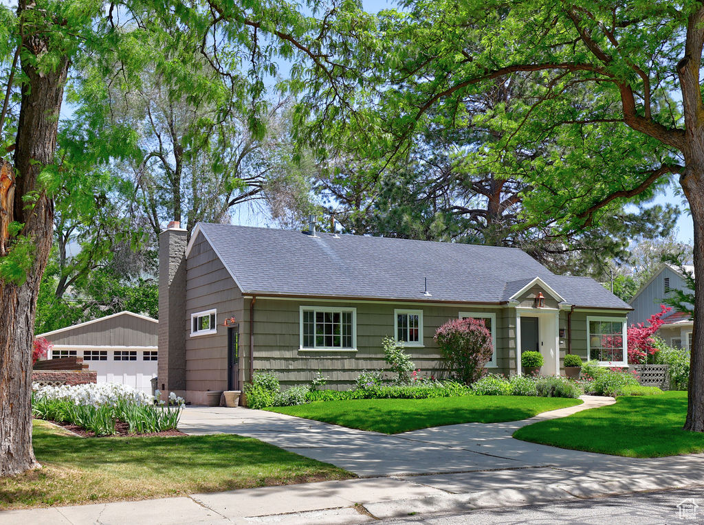 Single story home featuring a chimney, a detached garage, a front yard, and roof with shingles