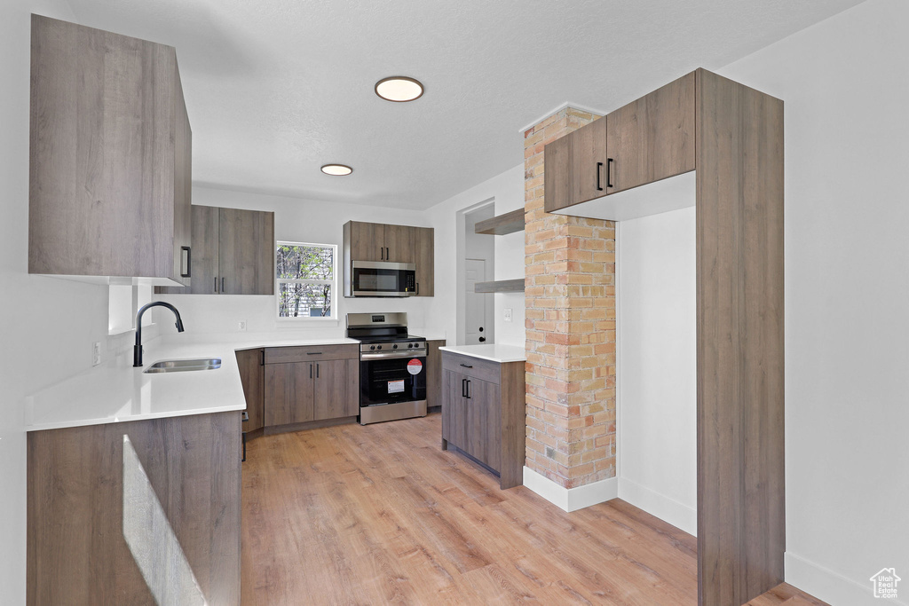 Kitchen featuring appliances with stainless steel finishes, a sink, light countertops, light wood-style flooring, and recessed lighting