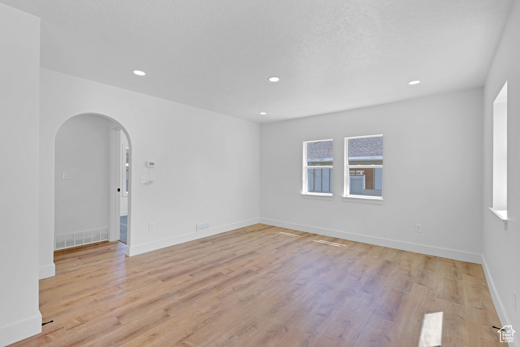 Empty room with arched walkways, light wood finished floors, recessed lighting, and baseboards