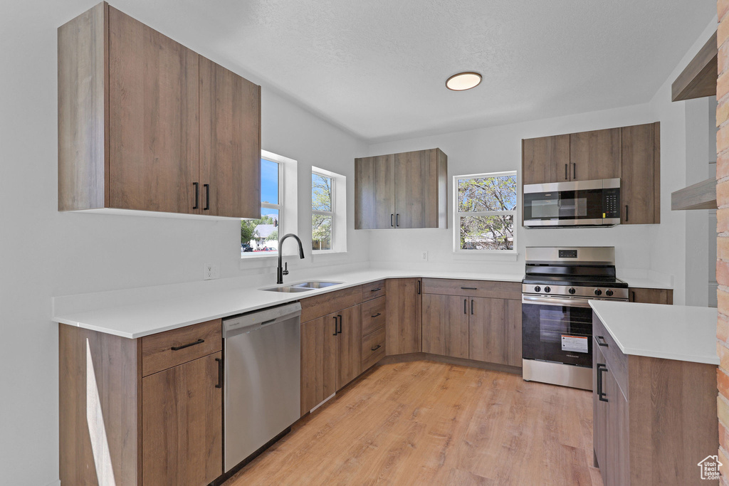 Kitchen with stainless steel appliances, a sink, light wood-type flooring, light countertops, and brown cabinets