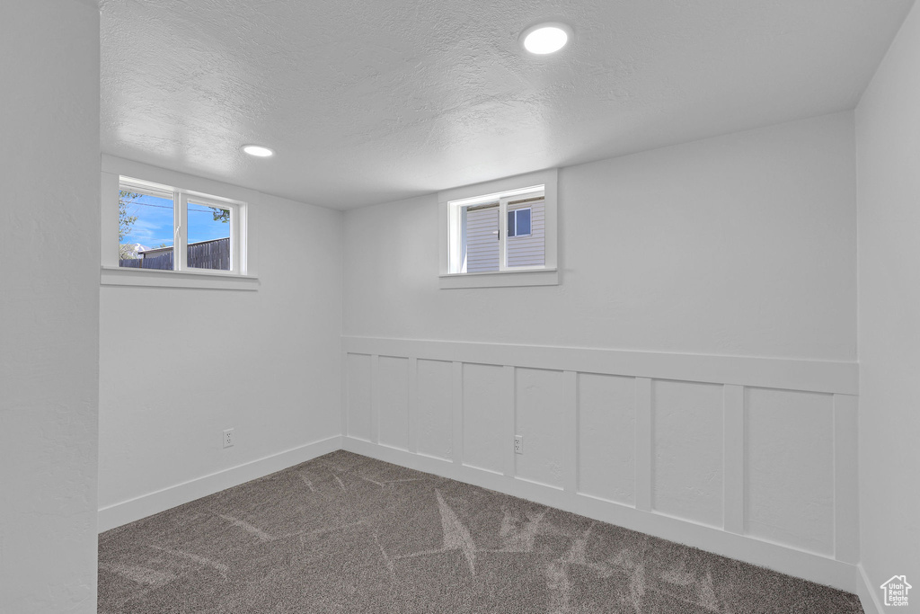 Below grade area with a textured ceiling, dark colored carpet, wainscoting, recessed lighting, and a decorative wall