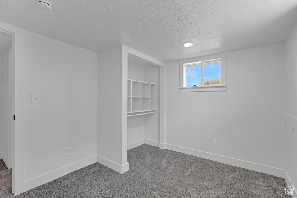 Basement with dark carpet, a textured ceiling, and baseboards