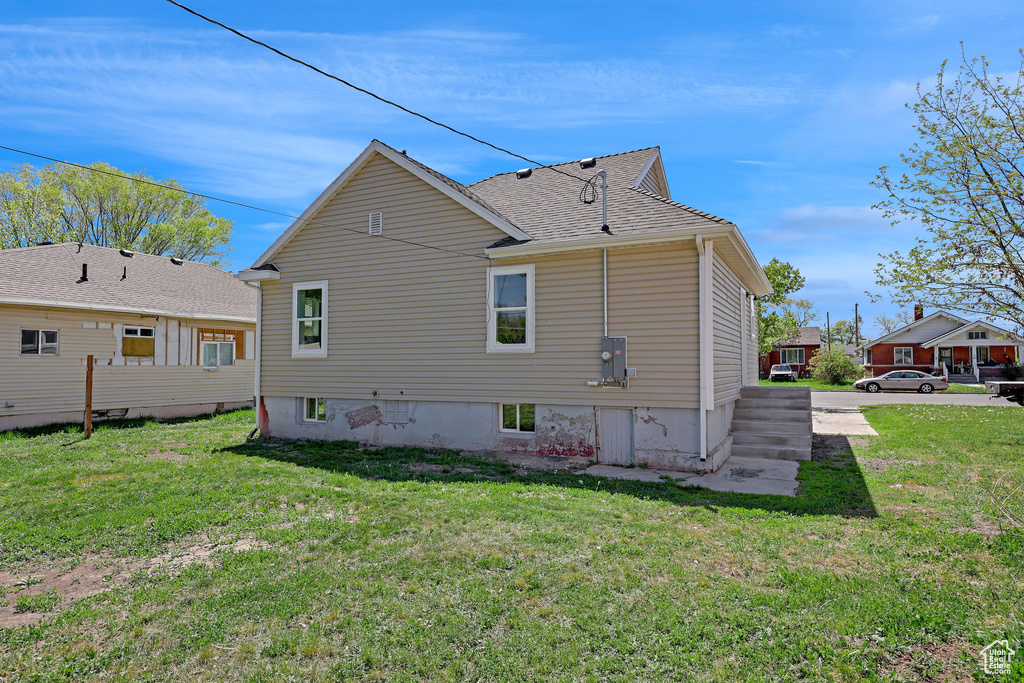 Rear view of property featuring a lawn and roof with shingles