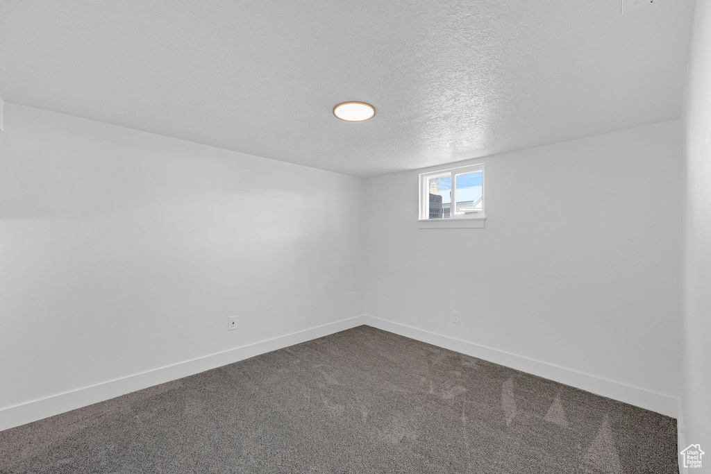 Spare room featuring dark colored carpet, baseboards, and a textured ceiling