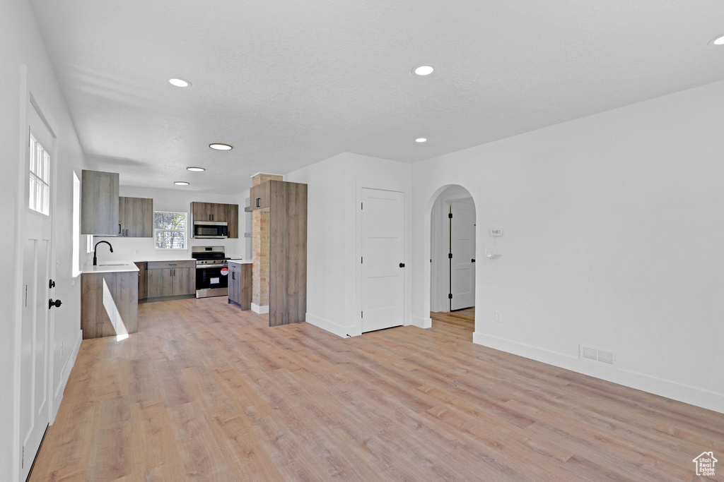 Unfurnished living room featuring recessed lighting, arched walkways, light wood finished floors, and baseboards