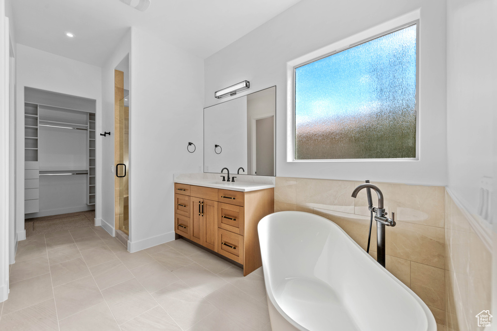 Full bathroom featuring a stall shower, a walk in closet, vanity, and a soaking tub