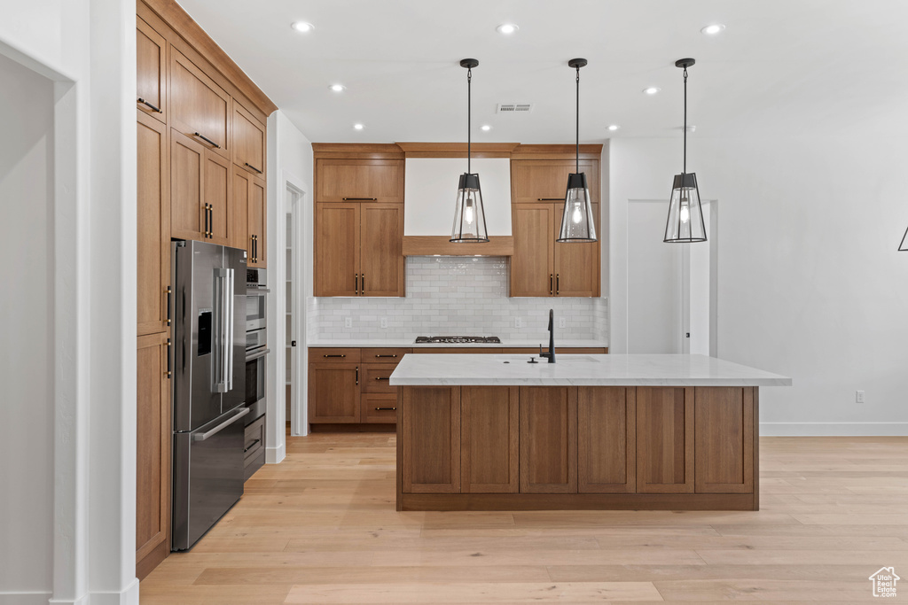 Kitchen with appliances with stainless steel finishes, extractor fan, tasteful backsplash, brown cabinetry, and light wood-style flooring