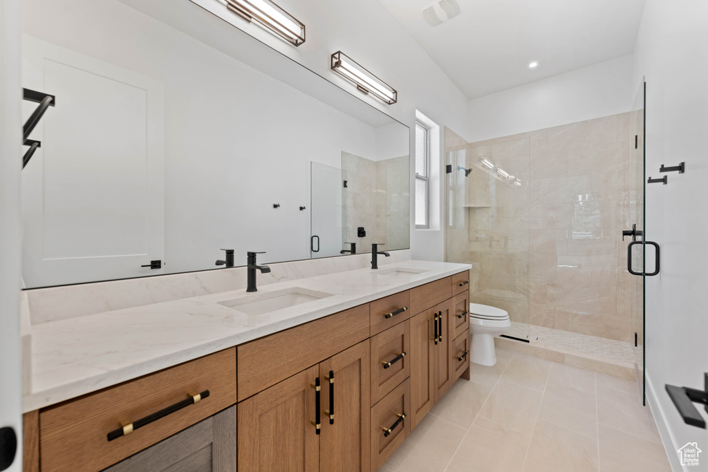 Bathroom featuring a shower stall, toilet, double vanity, and tile patterned floors