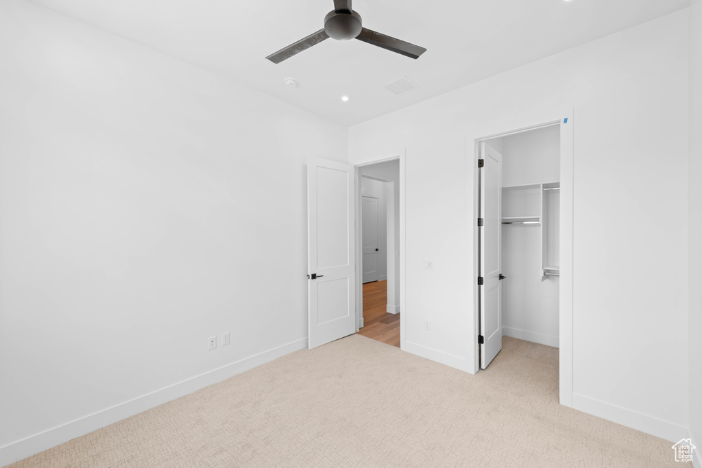 Unfurnished bedroom with light colored carpet, baseboards, a walk in closet, and ceiling fan