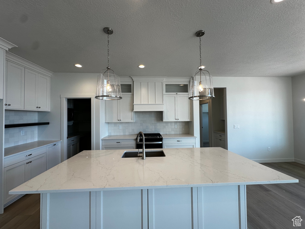 Kitchen with dark wood-style floors, decorative backsplash, an island with sink, white cabinetry, and a sink