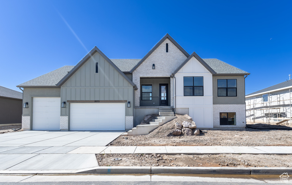 Modern inspired farmhouse featuring brick siding, a garage, concrete driveway, and roof with shingles