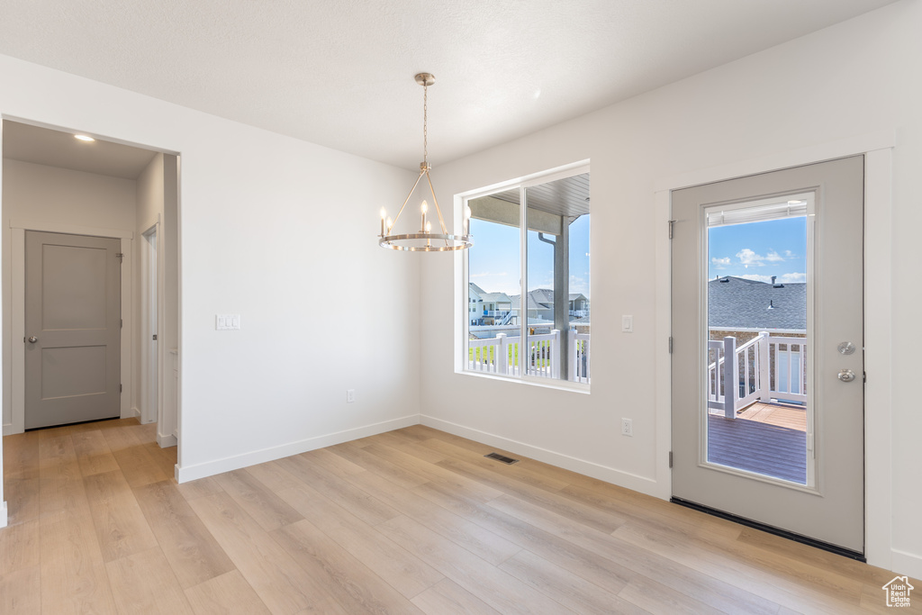 Unfurnished dining area featuring a chandelier, light wood finished floors, and baseboards