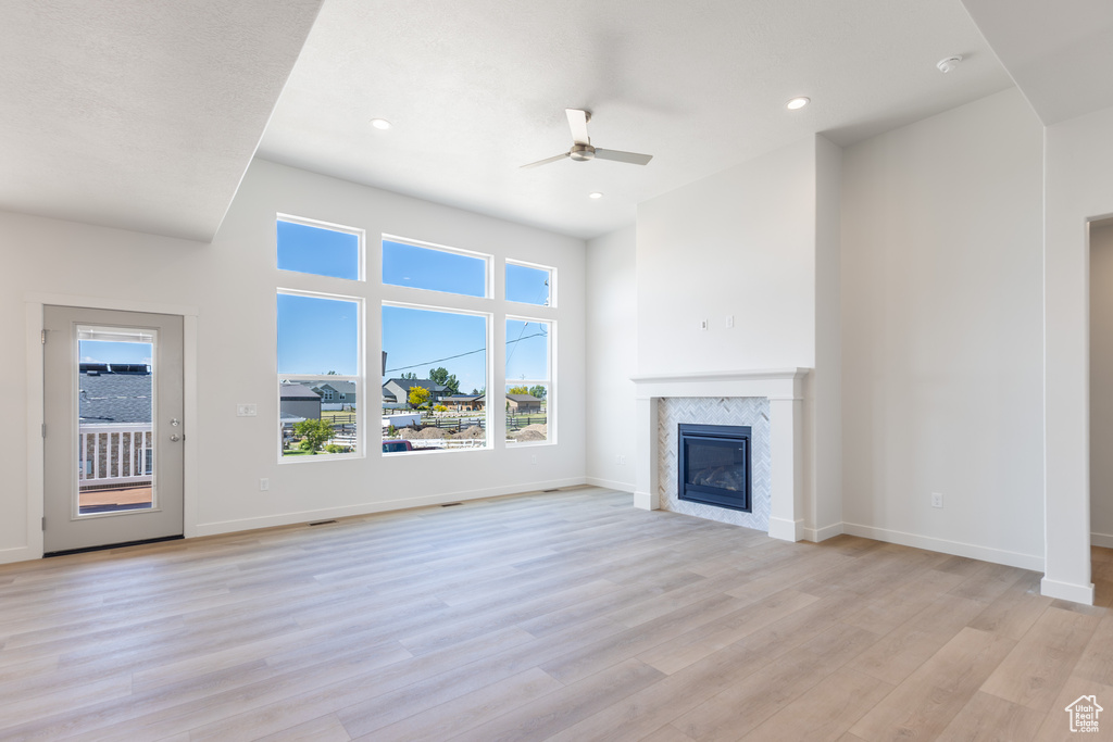 Unfurnished living room featuring a ceiling fan, healthy amount of natural light, a premium fireplace, light wood-type flooring, and recessed lighting