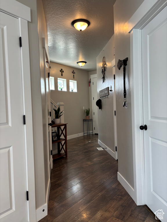 Hallway with dark wood-style floors, a textured ceiling, and baseboards