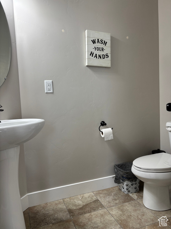 Half bathroom with baseboards, toilet, stone finish flooring, and a sink