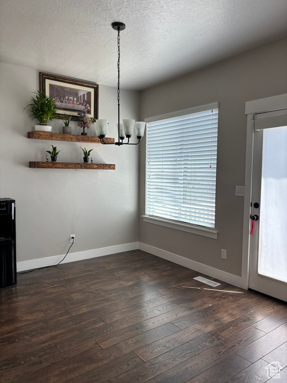 Unfurnished dining area with dark wood-style floors, a chandelier, baseboards, and a textured ceiling