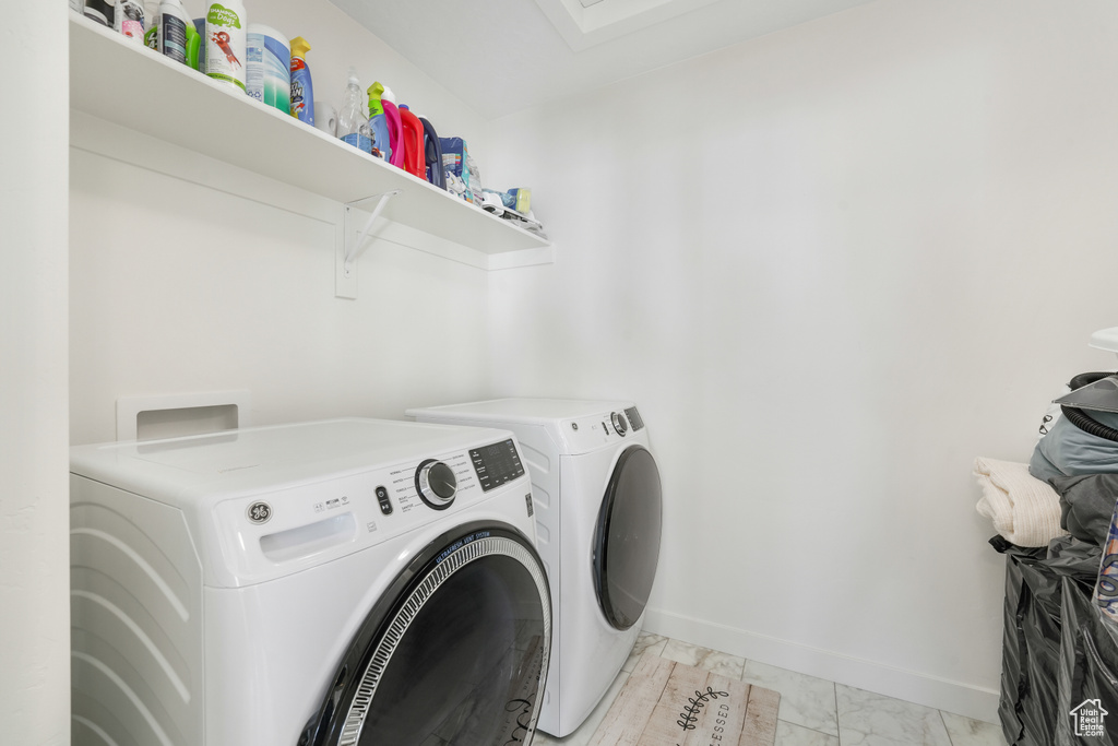 Clothes washing area featuring washing machine and clothes dryer, light marble finish flooring, and baseboards