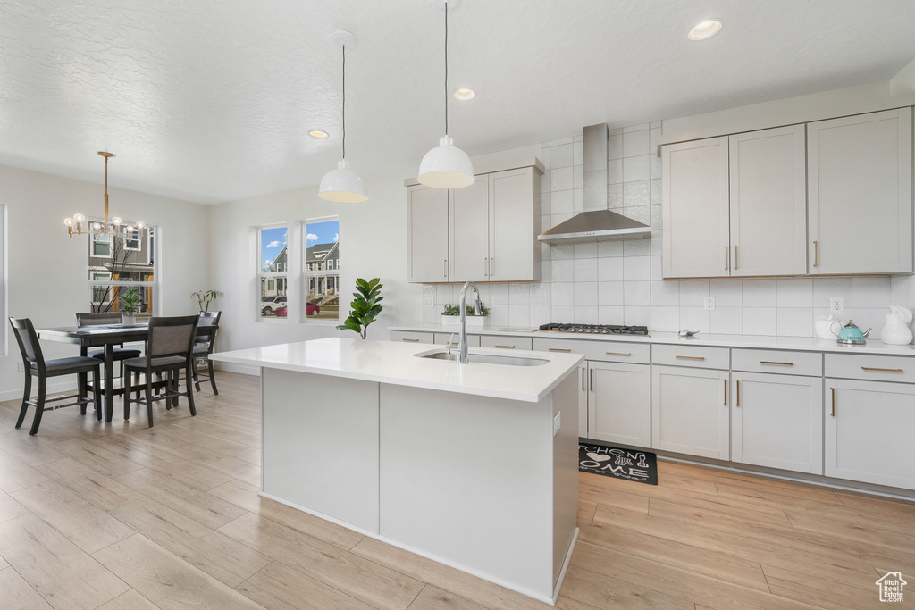 Kitchen with wall chimney exhaust hood, a sink, light countertops, light wood-type flooring, and backsplash